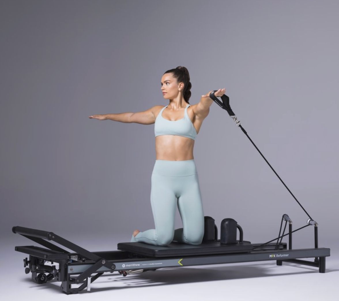 Woman kneeling on the Merrithew MPX Reformer Package pulling the strap