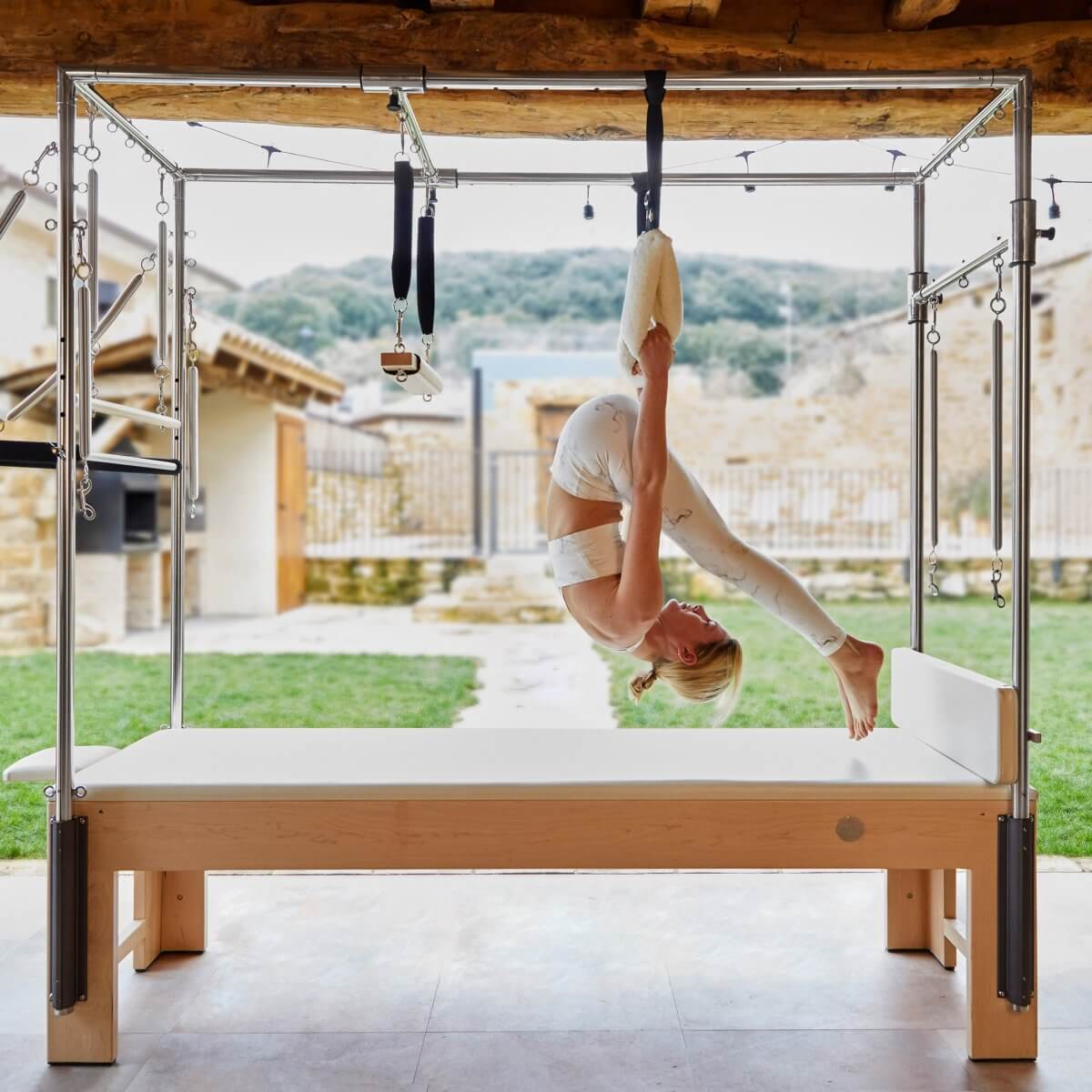 Woman performing an inverted hang on the Elina Pilates Wooden Cadillac on a covered terrace