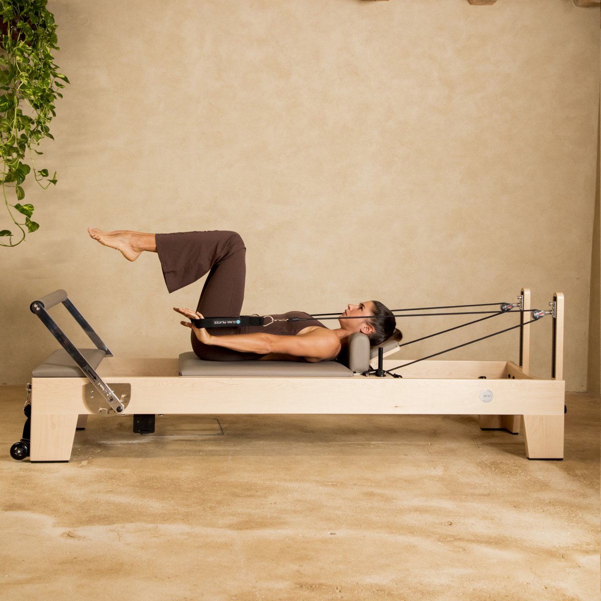 Woman performing a supine leg exercise on the Elina Pilates Elite Reformer in a warm-toned studio