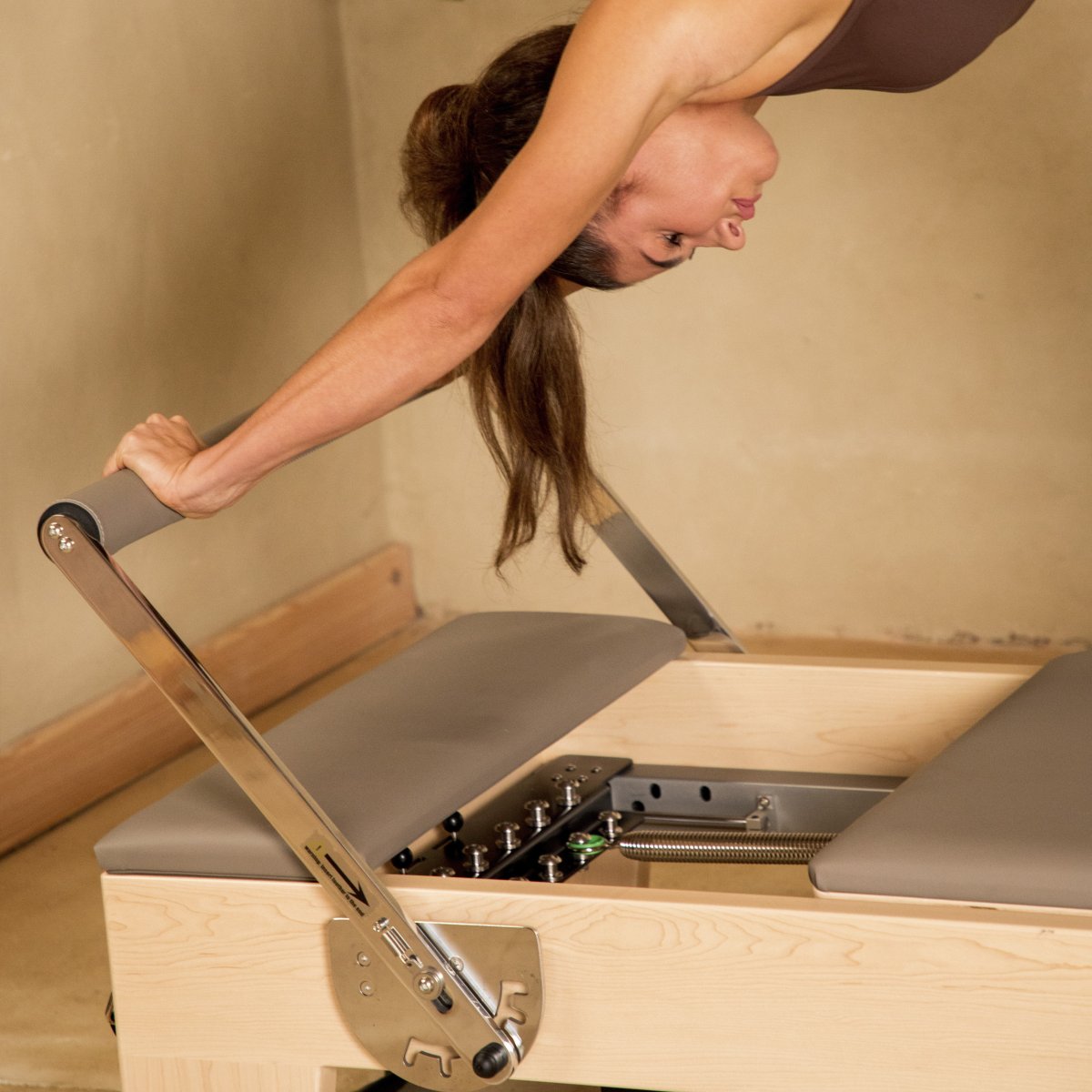 Woman adjusting the footbar of the Elina Pilates Elite Reformer with the carriage panel open to show the springs