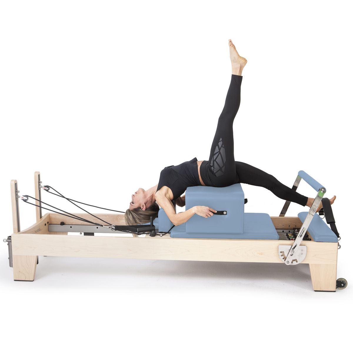 Woman performing a single-leg bridge on the Elina Pilates Elite Reformer with blue upholstery