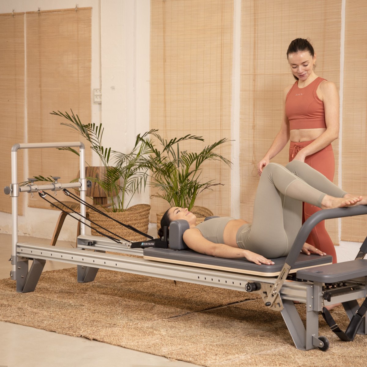 Instructor guiding a client on the Elina Pilates Nubium Reformer in a studio with plants